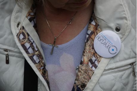 Donna con giacca chiara e spilletta sopra il petto con il logo oxygen, indossa una collana con croce.