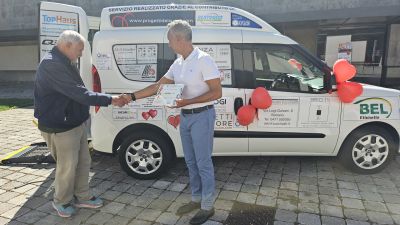 Due uomini si stringono la mano davanti all’auto decorata con loghi e palloncini rossi a forma di cuore.