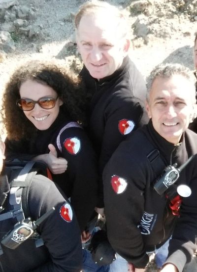 Gruppo di pellegrini radunati attorno alla grande statua bronzea del Cristo Risorto a Medjugorje, mentre toccano la scultura all’aperto.