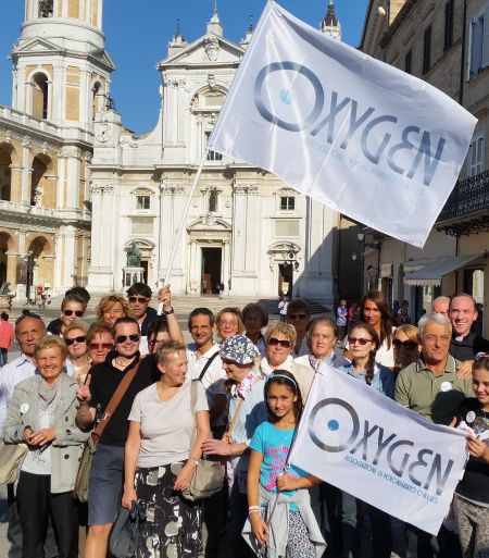 Gruppo di volontari dell’associazione Oxygen riuniti in piazza con due bandiere dell’associazione ben visibili.